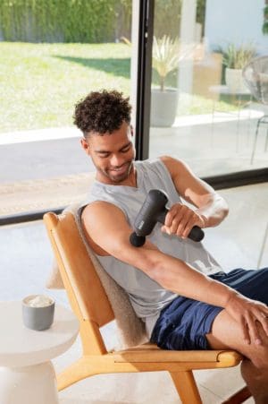 Man using HoMedics Therapist Select Percussion Massager for home muscle therapy and mobility support.