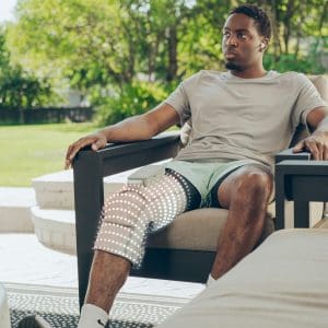 Man using HoMedics Modulair Compression Knee Wrap, glowing lights for home therapeutic pain relief.